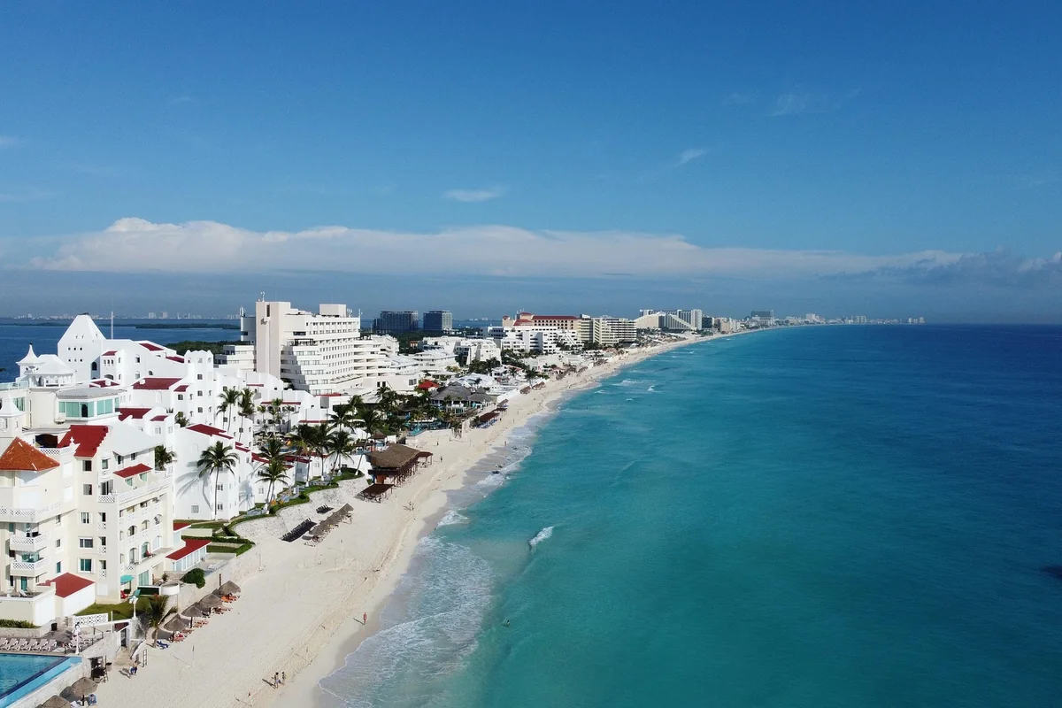 Aerial view of the hotel-lined Cancun coastline, white resort buildings between the lagoon and turquoise Caribbean water
