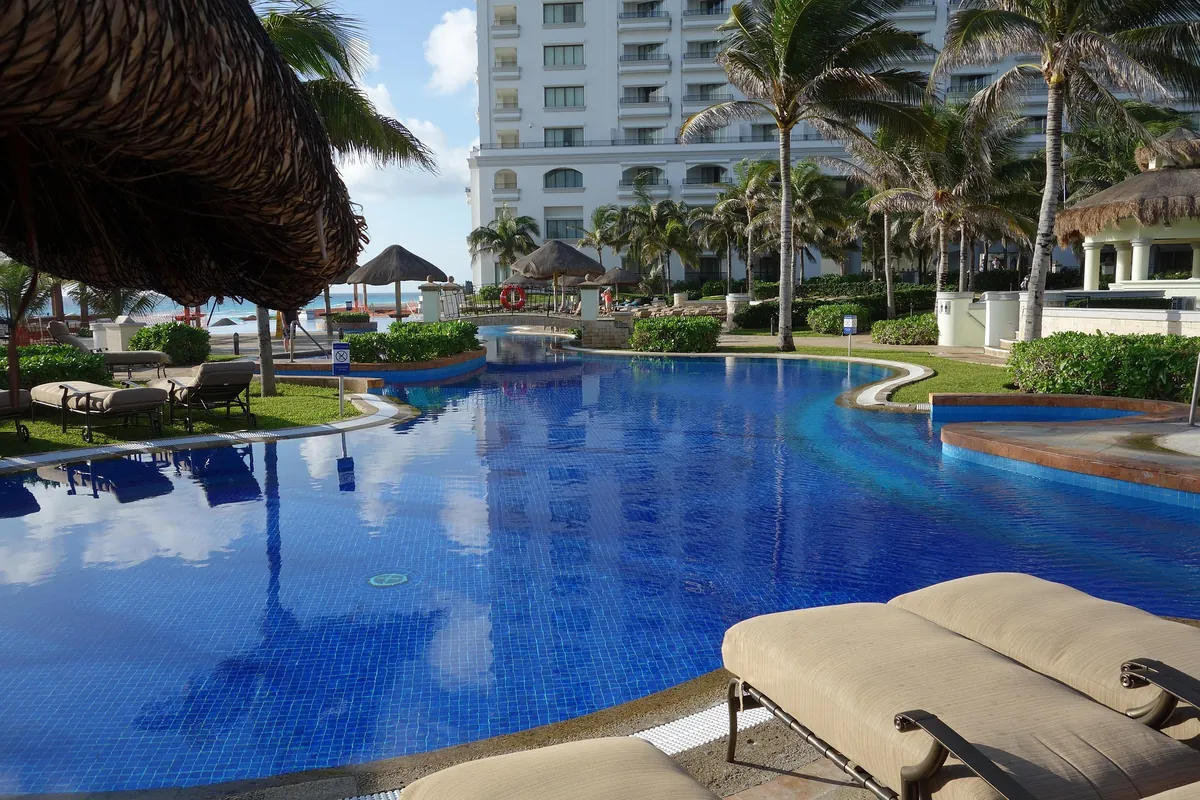 Poolside view at a beachfront resort in the Cancun hotel zone, with palapas and loungers