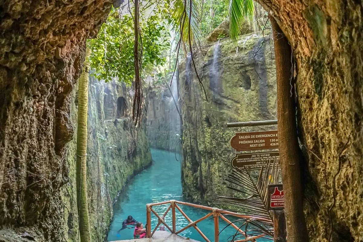 Turquoise cenote canyon at Xcaret, with rock walls, hanging vines, and a wooden walkway