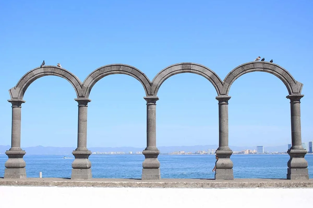The stone arches sculpture on Puerto Vallarta's malecon boardwalk, with the bay and coastline behind